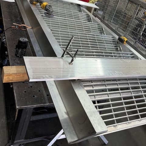 Long aluminum frame with bar grating panels on a welding table in the shop, bare mill finish
