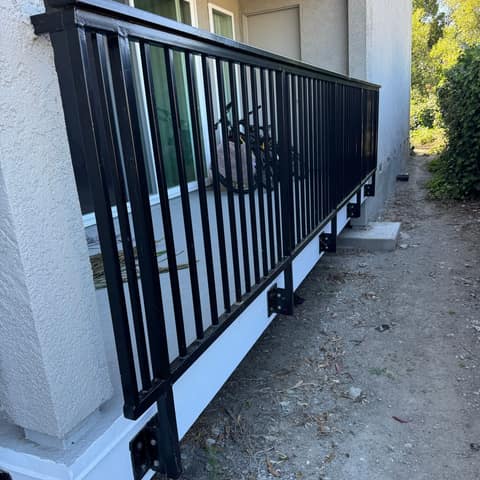 Black steel picket railing with bolted side-mount brackets along a ground-floor apartment patio.