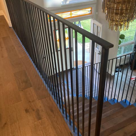 Dark bronze steel picket guardrail along an upstairs landing overlooking a stair and entry.