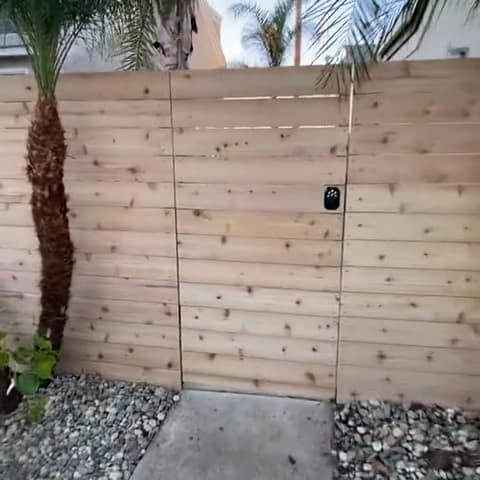Short video: walking up to a cedar privacy gate with a black keypad lock between matching fence panels.