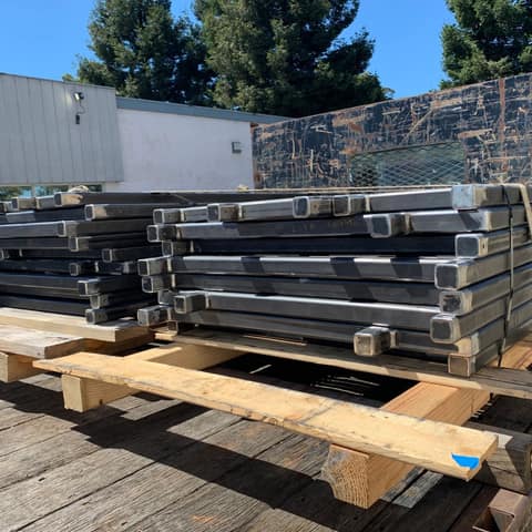 Stacks of welded square steel tube frames strapped to a flatbed trailer, bare unpainted steel