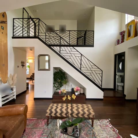 Black steel stair and loft railing with a geometric diagonal bar pattern in a two-story living room.