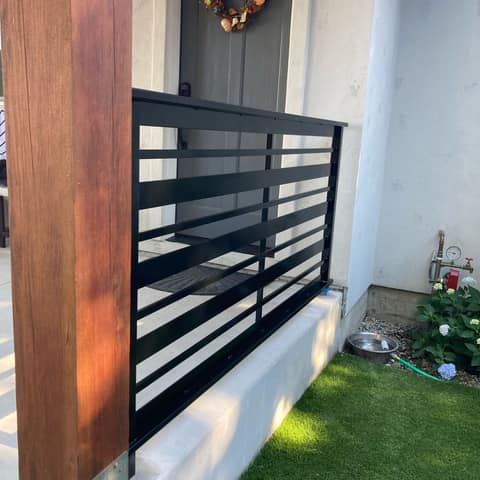 Black steel porch railing with horizontal flat bars of varied widths beside a wood post.