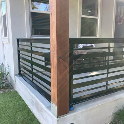 Black steel porch railing with horizontal flat bars wrapping the corner of a front porch.