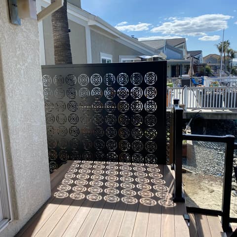 Black laser-cut steel privacy screen with a circle pattern casting shadows across a waterfront deck.