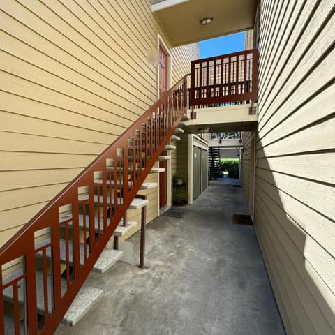 Rust-red laser-cut steel stair railing and upper guardrail with a vertical bar pattern in an apartment breezeway.