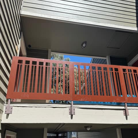 Rust-red laser-cut steel guardrail panels bolted to the edge of an apartment walkway.
