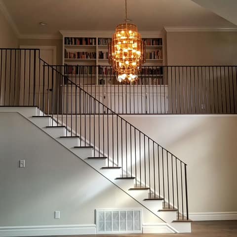 Dark steel picket stair and loft railing in a two-story room below a chandelier.