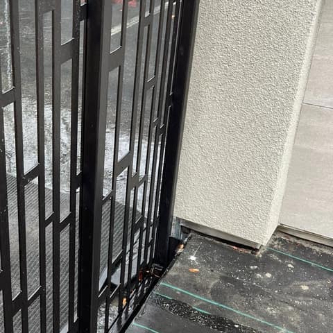 Black painted steel screen panel with an irregular pattern of rectangular openings, standing on wet pavement at a job site