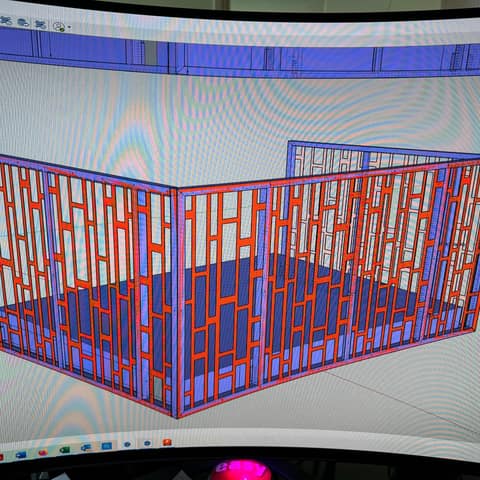 3D computer model of a decorative screen wall enclosure with an irregular pattern of rectangular openings, shown in red and blue