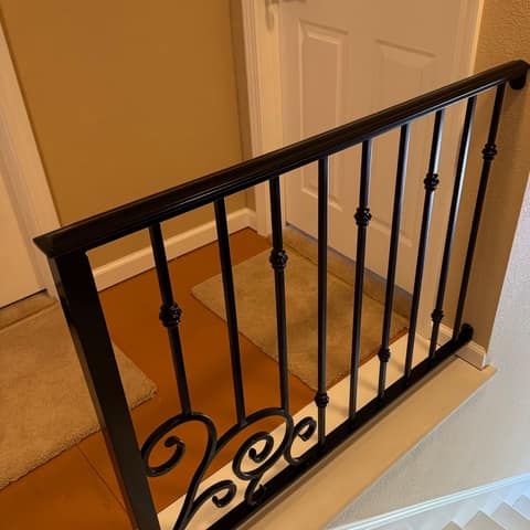 Matching black steel landing guardrail with knuckle-accent pickets and a scroll panel at the top of a stair.