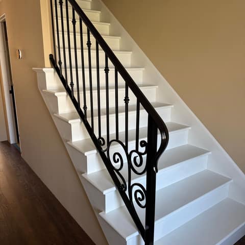 Black steel stair railing with knuckle-accent pickets, hand-formed scroll panel and a rolled handrail end.