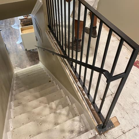 Dark bronze steel square-picket stair railing with a matching wall handrail at the top of an interior stair.