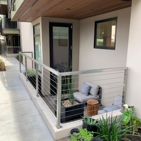 Brushed stainless steel patio railing with horizontal cable infill at a ground-floor apartment.
