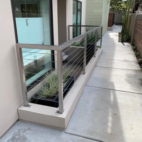 Brushed stainless steel patio railing with horizontal cable infill along an apartment walkway.