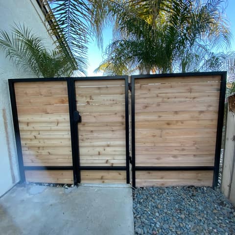 Black steel gate and fence frames with horizontal cedar board infill across a side yard.