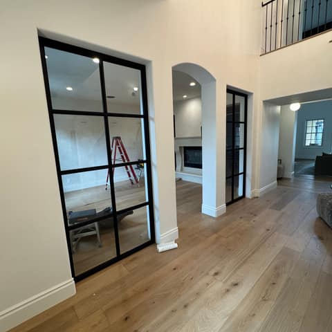 Two black steel-framed interior glass walls with divided panes in a two-story entry, with a black iron balcony railing above.