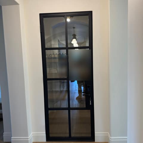 Black steel and glass interior door with eight divided panes, opening to a home wine room.