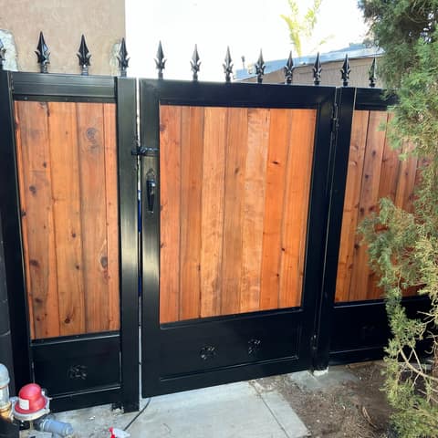 Black steel side gate and fence frames with redwood board infill, spear-point finials and decorative rosettes.