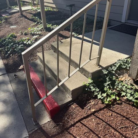 Tan steel picket handrail on three concrete entry steps at an apartment.