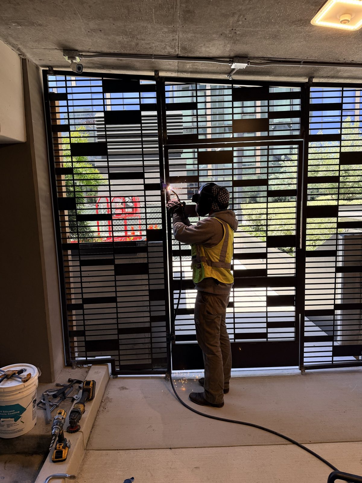 Welder in a safety vest welding a black decorative bar screen gate in a parking garage