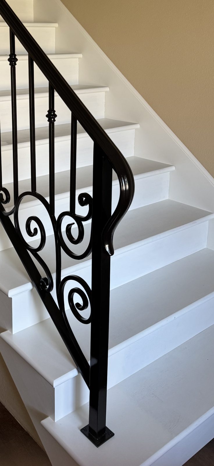 Black interior stair railing with scrollwork and a curved handrail end on white stairs