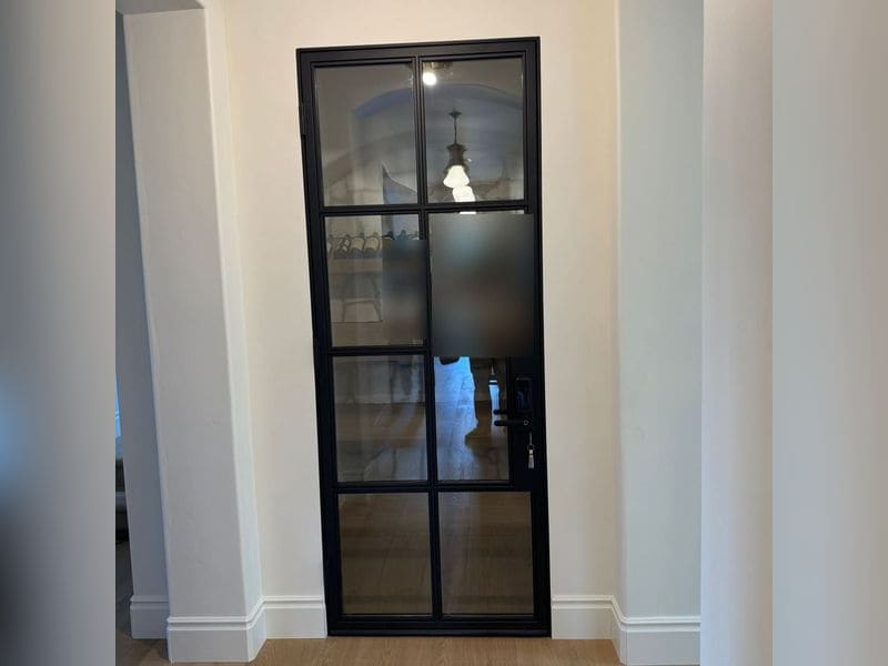 Black steel and glass interior door with eight divided panes, opening to a home wine room.
