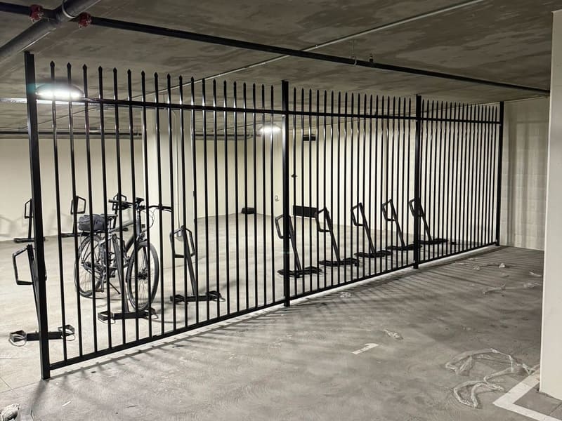 Black painted picket security fence enclosing a bike storage area in a concrete parking garage