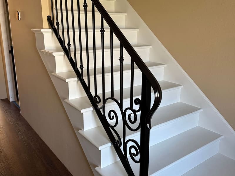 Black steel stair railing with knuckle-accent pickets, hand-formed scroll panel and a rolled handrail end.