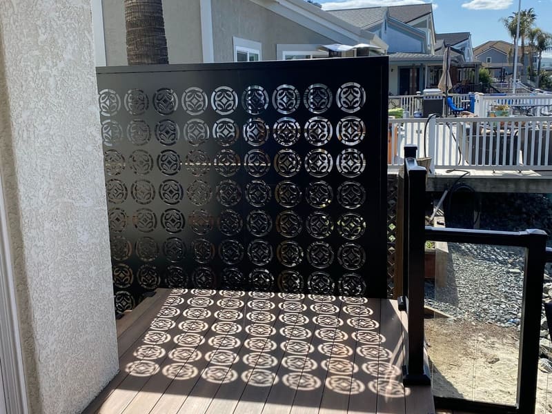 Black laser-cut steel privacy screen with a circle pattern casting shadows across a waterfront deck.