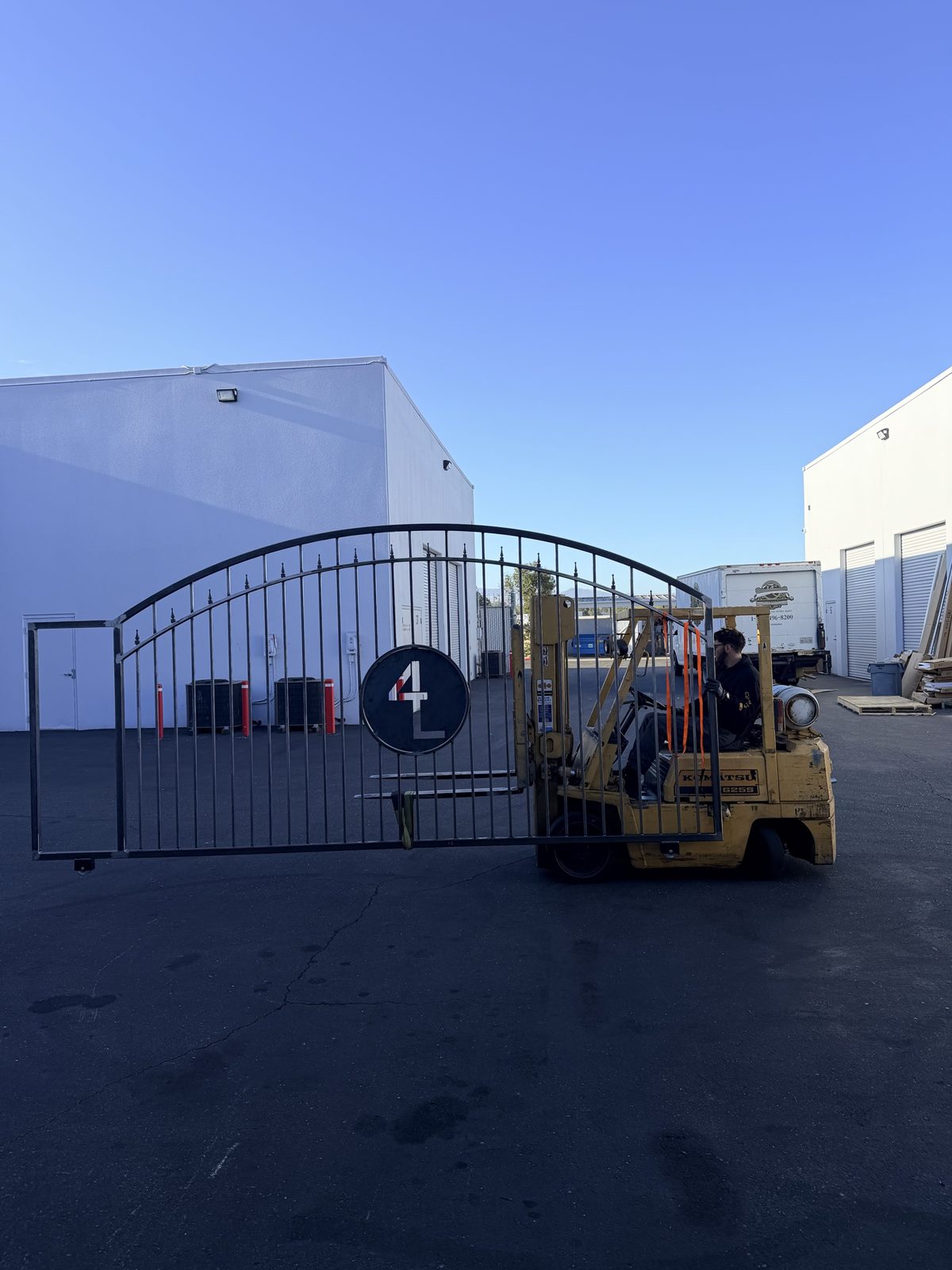 Large arched steel sliding gate carried on a forklift outside the shop